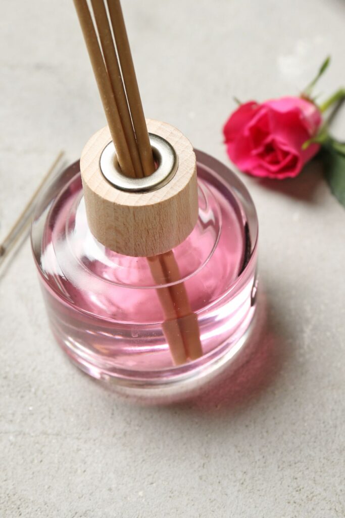 A aroma therapy diffuser bottle with pink liquid next to w pink rose.