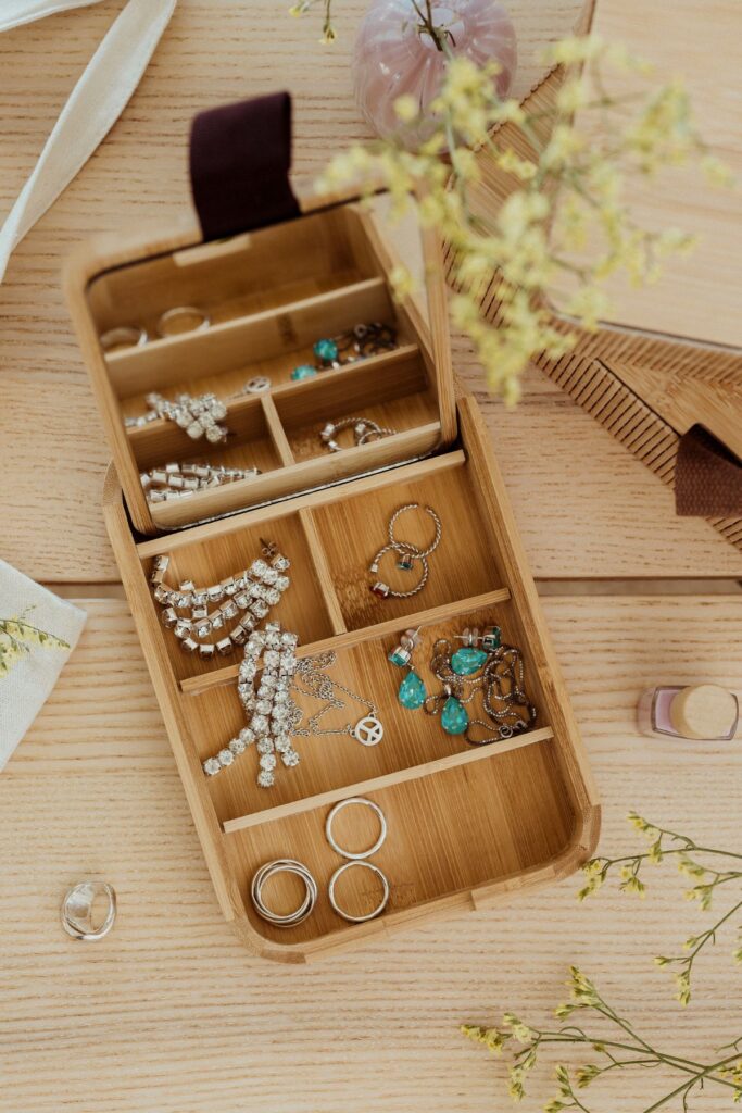 A wooden jewelry box organizer filled with jewelry on a table with flowers.