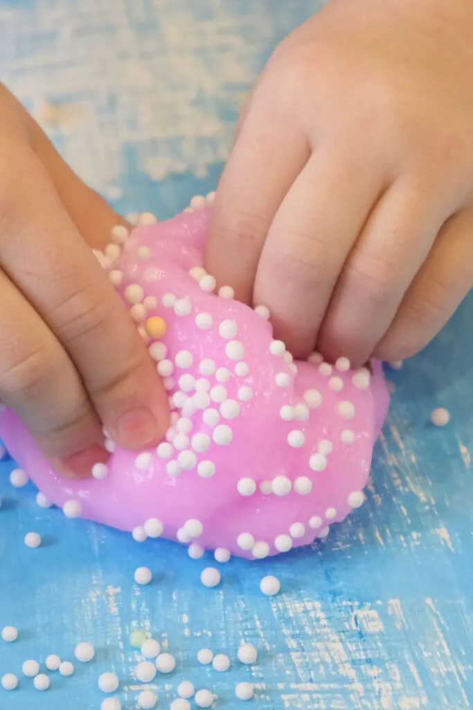 Small hands play with pink slime with white beads on a blue surface.