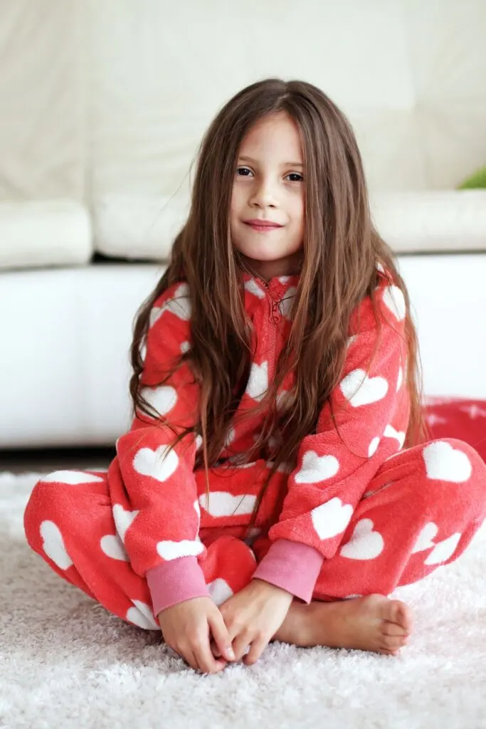 A girl wearing red pajamas with white hearts sits on the floor.