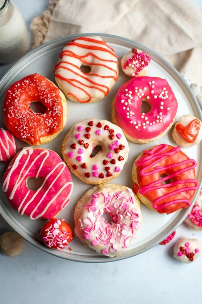A plate of donuts decorated with pink, red, and white icing and Valentine's Day sprinkles.