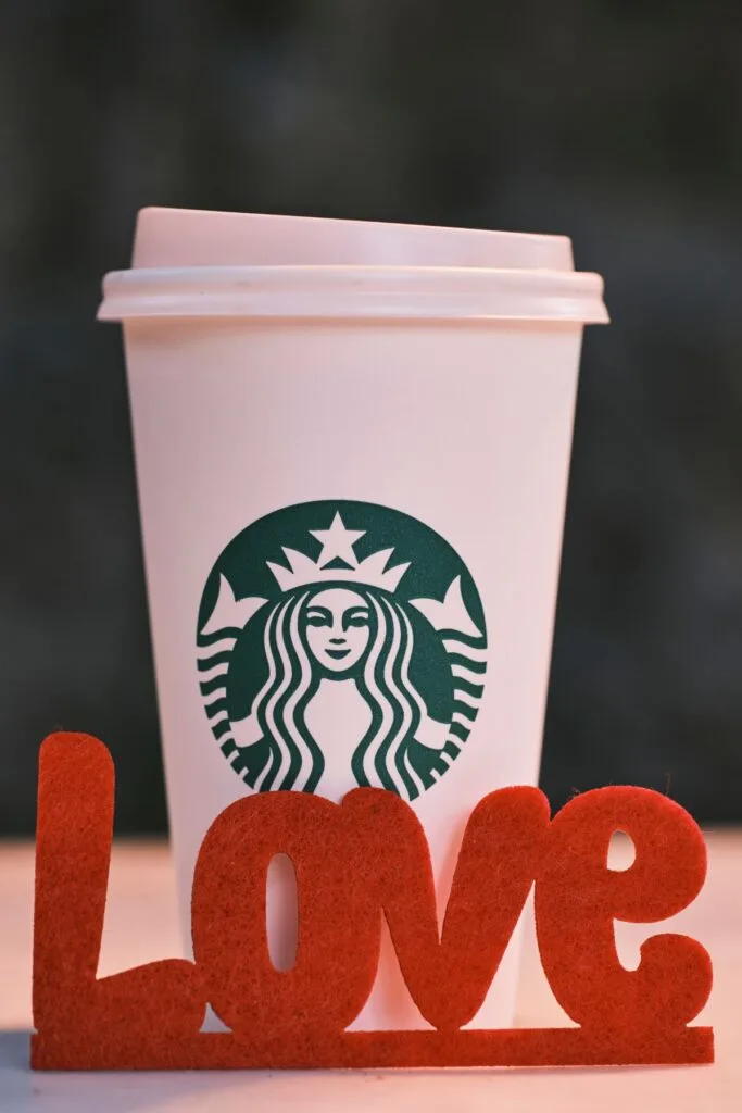 A Starbucks cup on table with the word "love" in front in red felt letters.