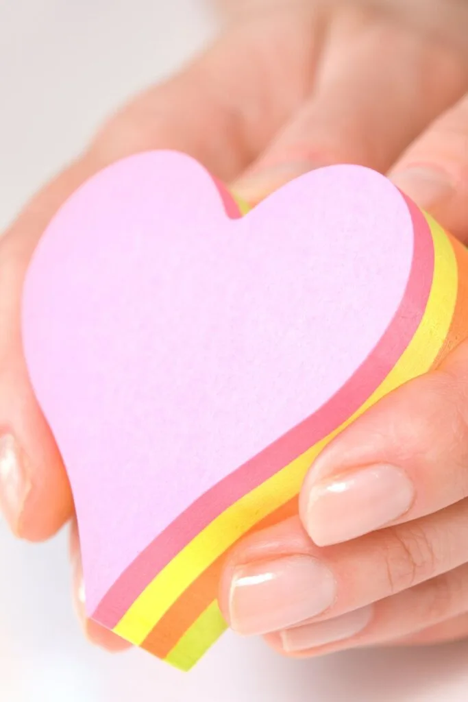 A woman's hands hold a stack of heart-shaped sticky notes.