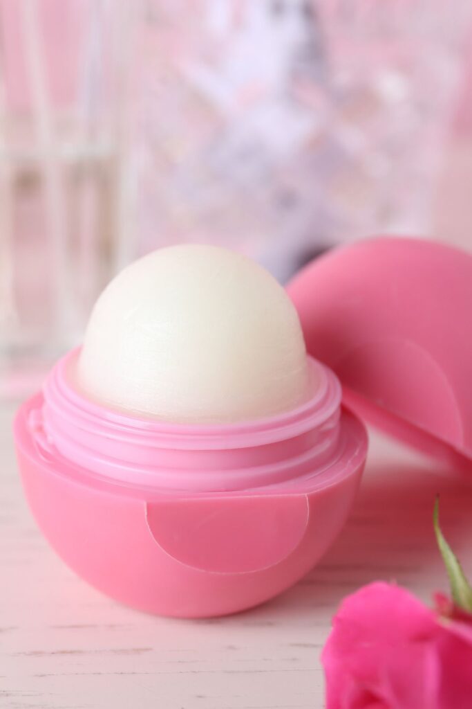 A round pink container of lip balm sits open on a table.