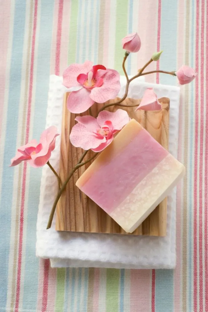 A pink and white bar of soap with pink flowers on a stripped cloth surface.