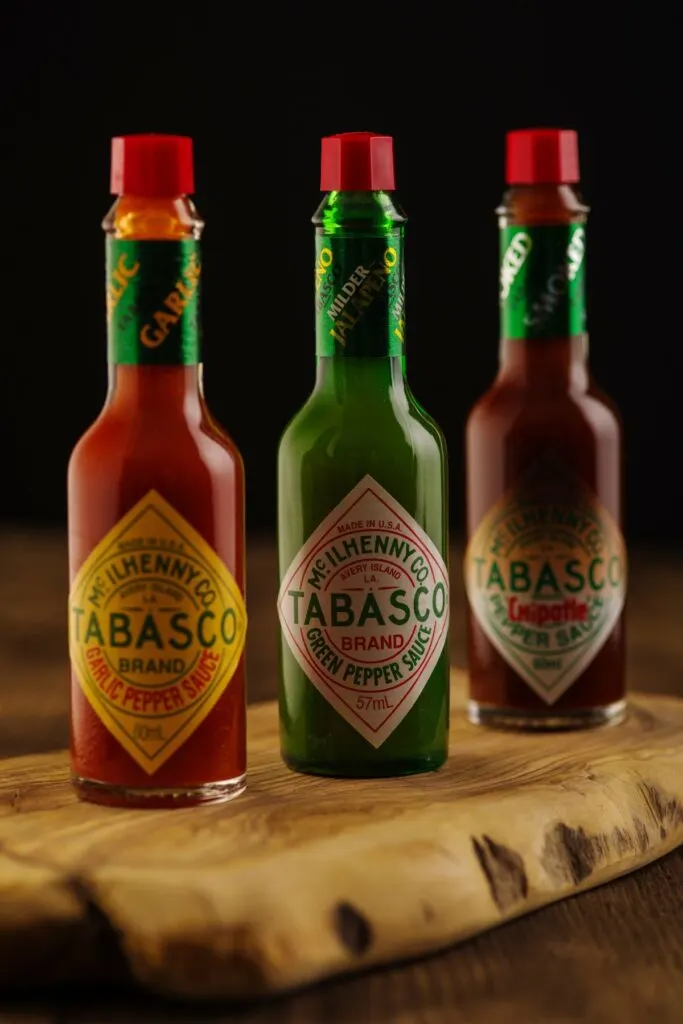 Three bottles of different tabasco sauce varieties on a wooden cutting board.