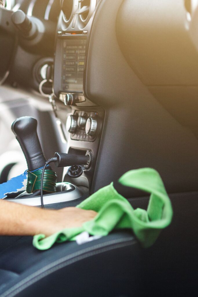A hand wipes down the interior of a car with a green cloth.