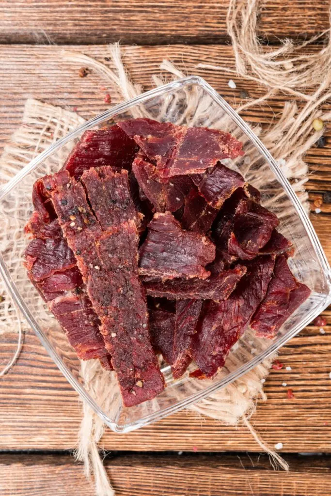 Beef jerky in a clear container on a burlap cloth.