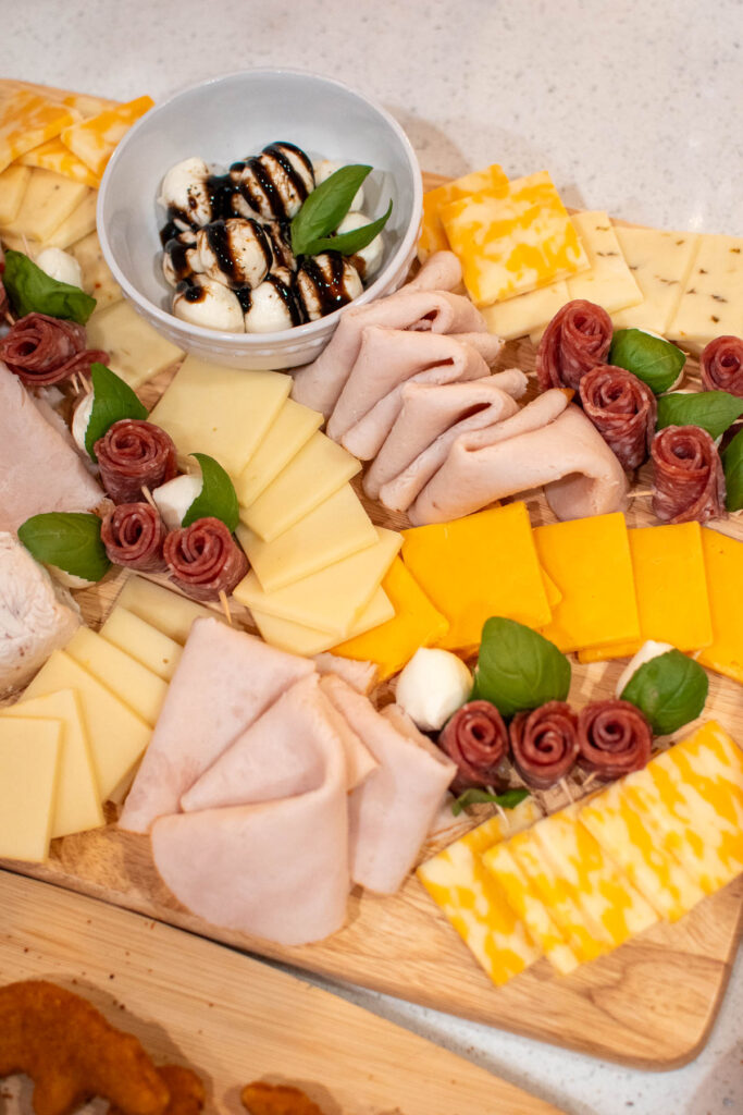 Meat and cheese board with turkey, cheese slices, salami roses, and mozzarella balls.