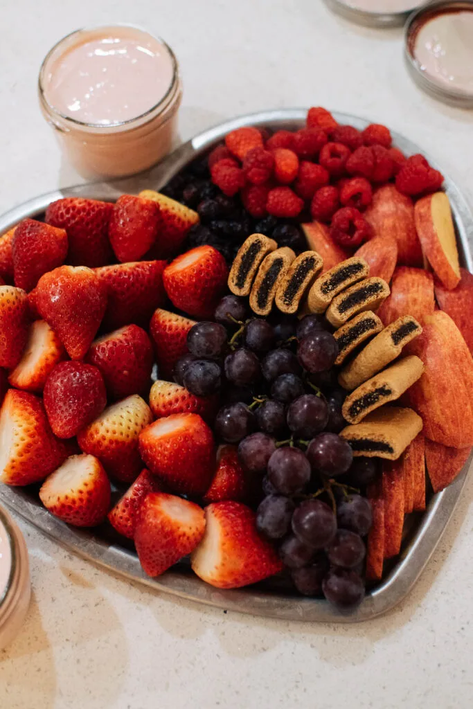 Heart shaped tray with fresh strawberries, grapes, raspberries, apples, and fig cookies.
