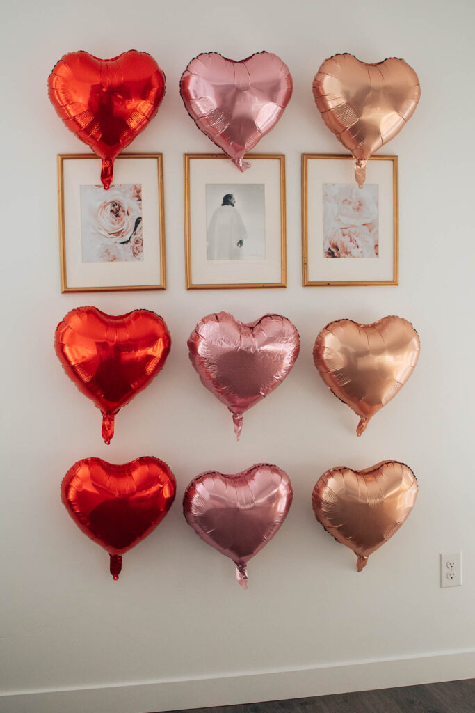 Pink and red heart-shaped balloons attached to wall around 3 picture frames.