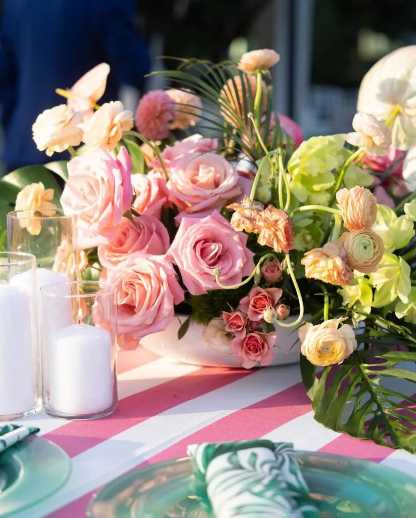 A party table outside with a pink and white striped tablecloth and flowers.