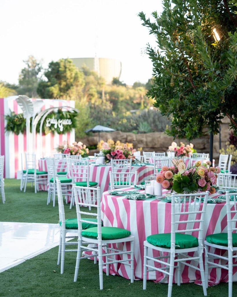 Party tables outside with pink and white striped tablecloths and floral arrangements.