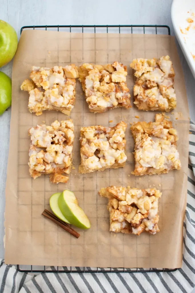 Apple streusel bars with green apple slices and cinnamon sticks on parchment paper.