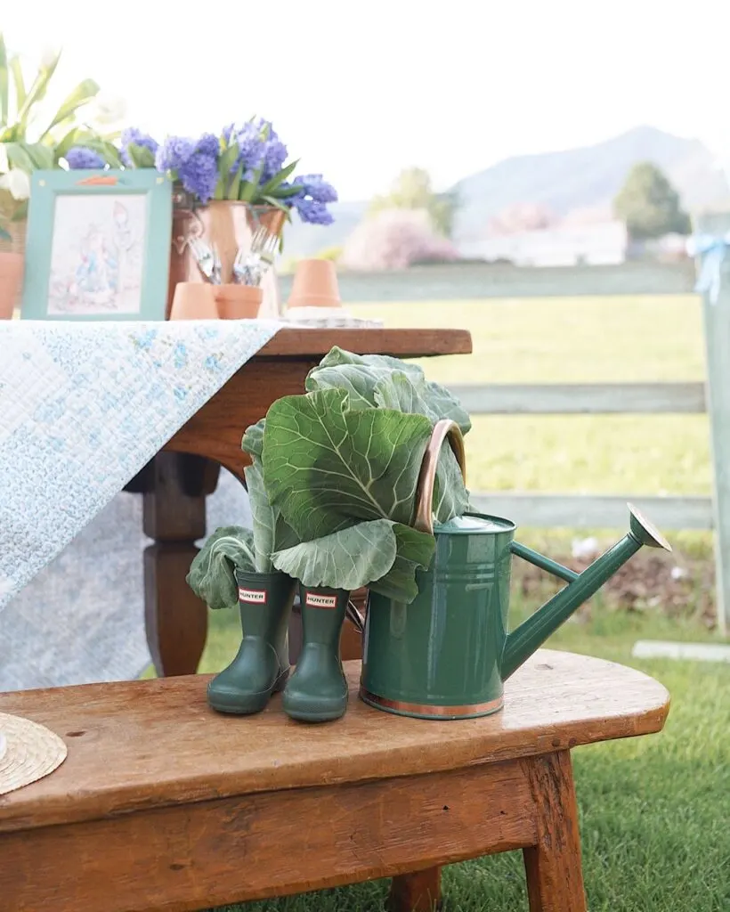 A party gift table with a wooden bench with garden boots and a watering can.