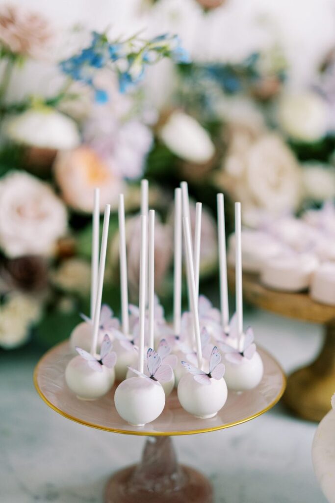 White cake pops with purple butterflies on a cake stand.