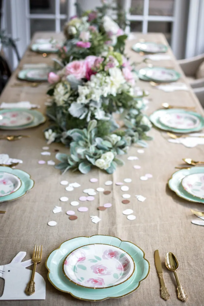 A party table with flower arrangements in the center and confetti.