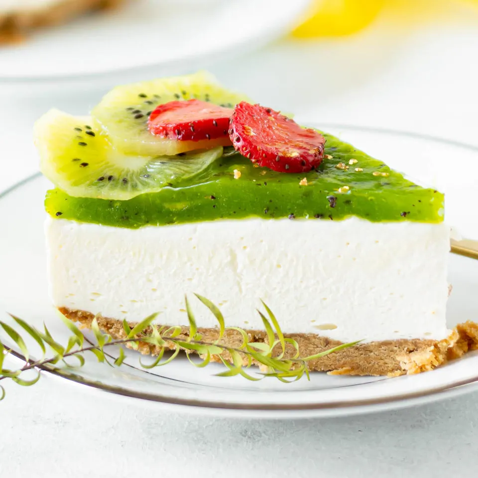 A slice of kiwi cheesecake on a white plate with kiwi and strawberry garnish.