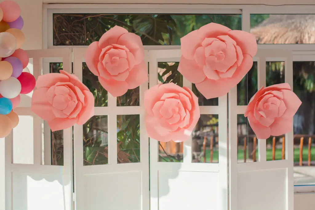 Pink paper flowers decorate a backdrop made from old doors with glass pane windows.
