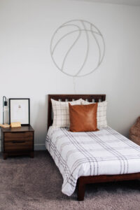 Basketball themed bedroom decor with brown leather pillow on bed and LED basketball light on wall.